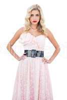 Stern blonde model in pink dress posing hands on the hips and lo