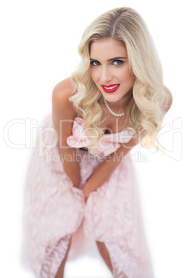 Smiling blonde model in pink dress posing hands on the thighs