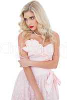 Concentrated blonde model in pink dress posing holding her arm