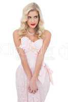 Concentrated blonde model in pink dress posing holding her hands