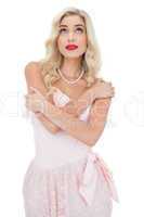 Pensive blonde model in pink dress posing holding her shoulders