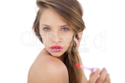 Thoughtful brunette model applying gloss on her lips