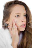 Thoughtful brunette in bathrobe rubbing her cheek with cream