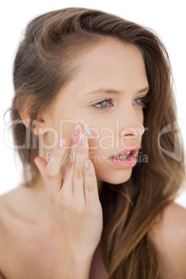 Attractive brunette model rubbing her cheek with cream