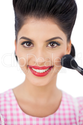 Smiling black hair model applying powder on her cheek