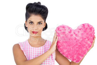 Unsmiling black hair model holding a pink heart shaped pillow