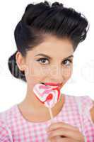 Cheerful black hair model chewing a heart shaped lollipop