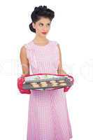 Pensive black hair model holding baking tray of cookies