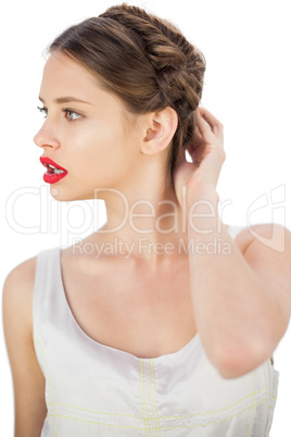 Puzzled model in white dress touching her hair and looking away