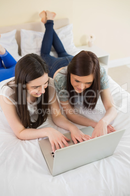 Friends using a laptop lying on bed