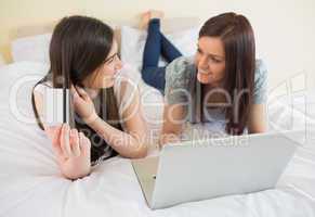 Happy friends using a laptop to shop online lying on bed