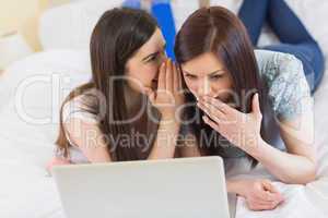 Girl telling a secret to her friend in front of laptop