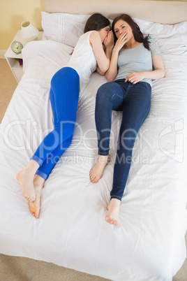 Smiling girl telling a secret to her friend lying on bed