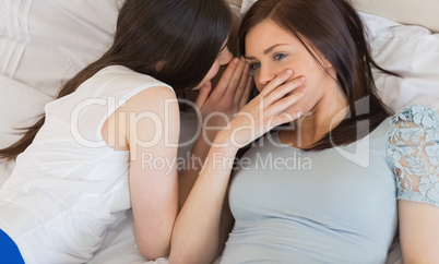 Pretty girl telling a secret to her friend lying on bed
