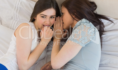 Happy girl telling a secret to her friend lying on bed
