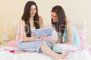 Girls in pajamas talking on bed using a tablet