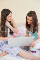 Cheerful friends in pajamas talking on bed using a laptop