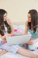 Smiling friends in pajamas talking on bed using a laptop