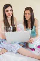 Smiling friends in pajamas talking on bed using a laptop looking