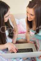 Happy friends in pajamas using a laptop on bed