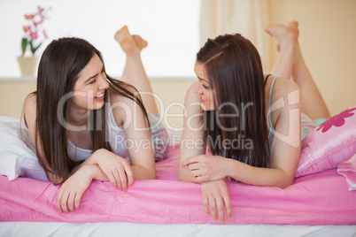 Smiling friends in pajamas chatting on bed