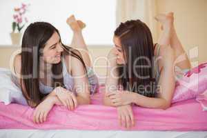 Smiling friends in pajamas chatting on bed