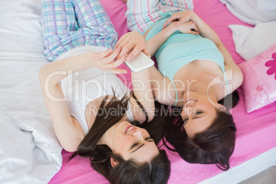 Smiling friends in pajamas laughing on bed