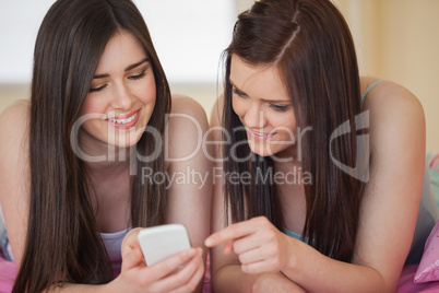 Happy friends in pajamas looking at smartphone on bed