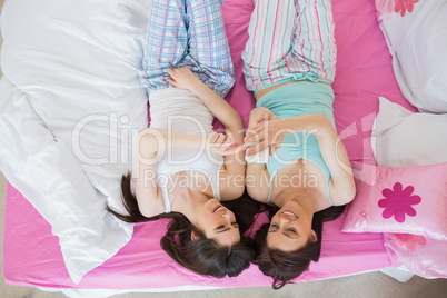 Pretty friends in pajamas looking at smartphone on bed