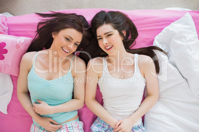 Smiling friends in pajamas looking at camera on bed