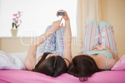 Friends in pajamas looking at smartphone on bed