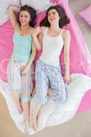 Close friends in pajamas lying on bed and laughing