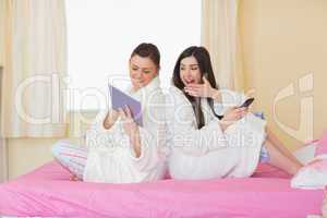 Two friends wearing bathrobes sitting back to back looking at ta