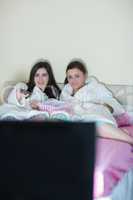 Two happy friends wearing bathrobes watching tv on bed