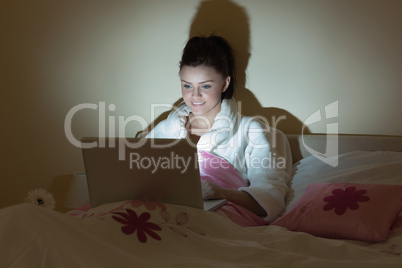 Pretty teen wearing bathrobe using her laptop in the dark