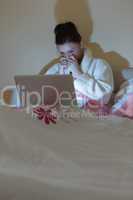 Pretty teen wearing bathrobe watching her laptop in the dark