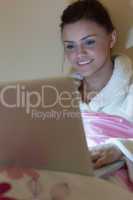 Pretty teen wearing dressing gown using her laptop in the dark