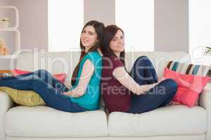 Two smiling friends sitting back to back on the sofa