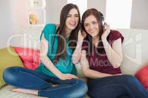 Smiling girl listening to music with her friend beside her on th