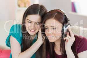 Cheerful girl listening to music with her friend beside her on t