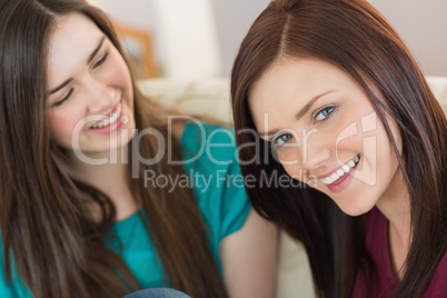 Two laughing friends sitting on the couch with one smiling at ca