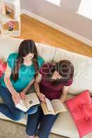 Two happy friends reading books on the couch
