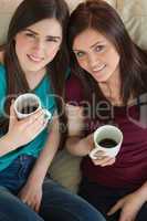 Two smiling friends having coffee and looking at camera on the c