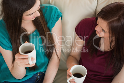 Two smiling friends having coffee and chatting on the couch