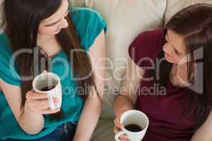 Two smiling friends having coffee and chatting on the couch