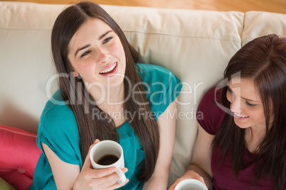 Two laughing friends having coffee on the couch