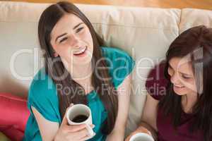 Two laughing friends having coffee on the couch