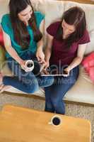 Two friends having coffee on the couch and using tablet