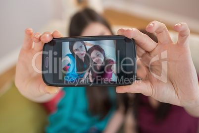 Two happy friends on the couch taking a selfie with smartphone