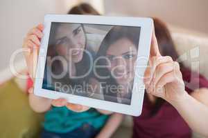 Two happy friends on the couch taking a selfie with tablet pc